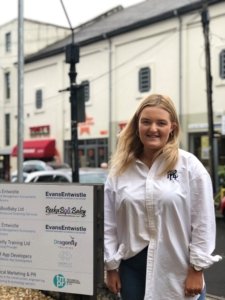 a blonde woman stood next to a sign with the TMPR logo on it