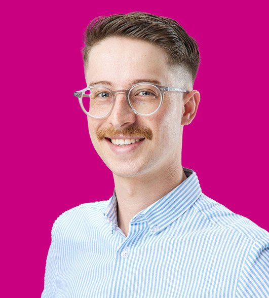 a headshot of Tom a man with a glasses and short brown hair