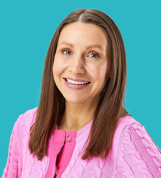 a headshot of grace a brunette woman in a pink cardigan